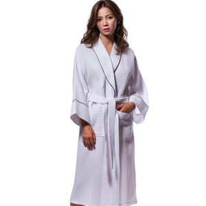 May include: White waffle weave bathrobe with a black trim around the collar, cuffs, and pockets. The robe has a shawl collar and a tie belt.