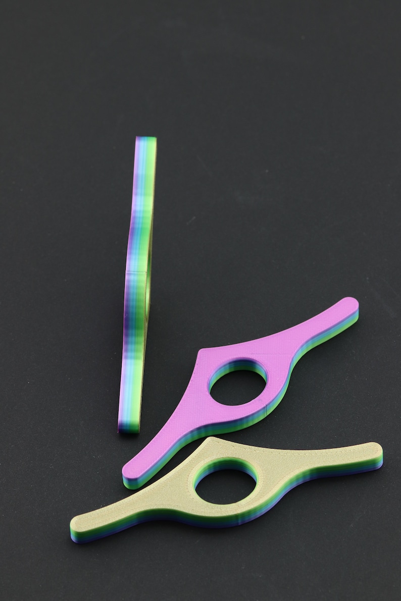 May include: Three colorful book page holders in shades of purple, green, and yellow. One is standing upright, while the other two are lying flat. Each has a circular opening and a layered design, perfect for keeping your place in a book.