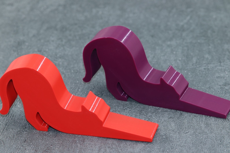 May include: Two doorstop cat figurines, one red and one purple, in a curled up position.