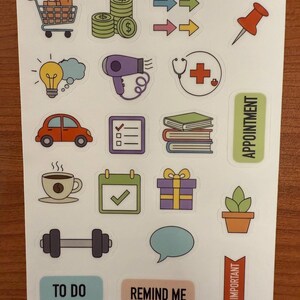 May include: A sheet of planner stickers featuring colorful illustrations of a shopping cart, money, arrows, a push pin, a lightbulb, a hairdryer, a stethoscope, a car, a checklist, books, a coffee cup, a calendar, a gift, a plant, a dumbbell, a speech bubble, and text that says "TO DO", "REMIND ME", and "IMPORTANT".