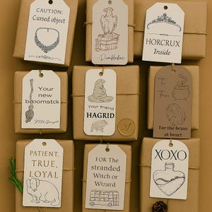 Puede incluir: Nueve regalos envueltos con etiquetas decorativas. Las etiquetas presentan ilustraciones y texto, incluyendo "CAUTION: Cursed object", "HORCRUX Inside" y "XOXO". Los regalos están atados con hilo.