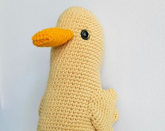 May include: A handmade, crocheted duck toy in a light yellow color with bright orange feet and beak. The duck has a round body, small wings, and a black button eye. This soft toy is a charming addition to a nursery or a child's room.