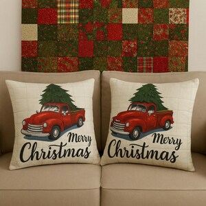 May include: Two beige Christmas throw pillows with a red vintage truck carrying a green Christmas tree. The pillows have the words "Merry Christmas" in black script. A patchwork quilt hangs in the background.