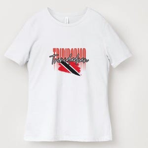 Pu&ograve; includere: T-shirt bianca con la scritta "Trinidadian" in un font stilizzato e il design della bandiera di Trinidad e Tobago. La bandiera &egrave; rossa, nera e bianca. La maglietta &egrave; un modello casual girocollo.