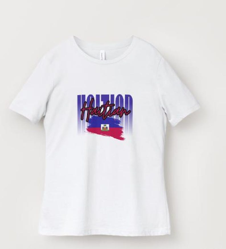 Pu&ograve; includere: T-shirt bianca con la scritta "Haitian" in un font stilizzato sopra una grafica della bandiera haitiana. Il design della bandiera include pennellate blu e rosse e lo stemma haitiano. La maglietta ha un girocollo e maniche corte.