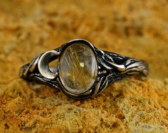 May include: A silver ring with a clear quartz stone with gold inclusions. The ring has a delicate, organic design.