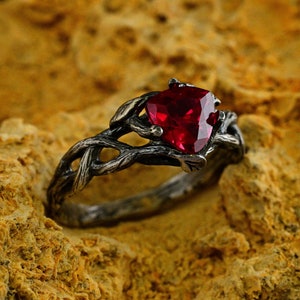 May include: A silver ring with a twisted branch design and a red heart-shaped gemstone.