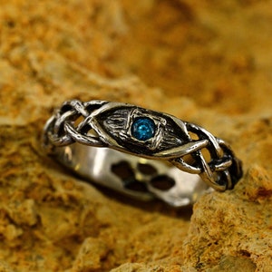 Può includere: Un anello d'argento con una pietra preziosa blu incastonata in un design a nodo celtico.