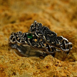 May include: A silver ring with a green gemstone set in a design of intertwined branches and leaves.