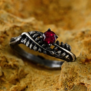 Pode incluir: Um anel de prata com uma gema vermelha engastada em um design de samambaia.