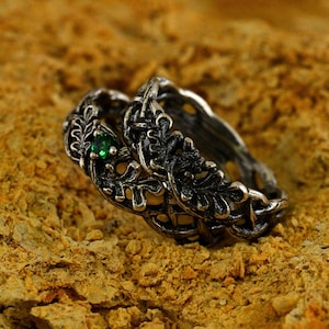 Könnte beinhalten: Zwei silberne Ringe mit einem komplizierten Blattdesign. Ein Ring hat einen grünen Edelstein.