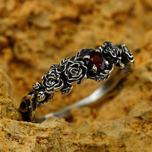 May include: A silver ring featuring a red gemstone set within a design of roses.