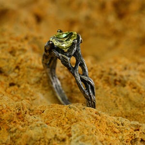Puede incluir: Un anillo de plata con un dise&ntilde;o de rama retorcida y una piedra preciosa verde engastada en el centro.