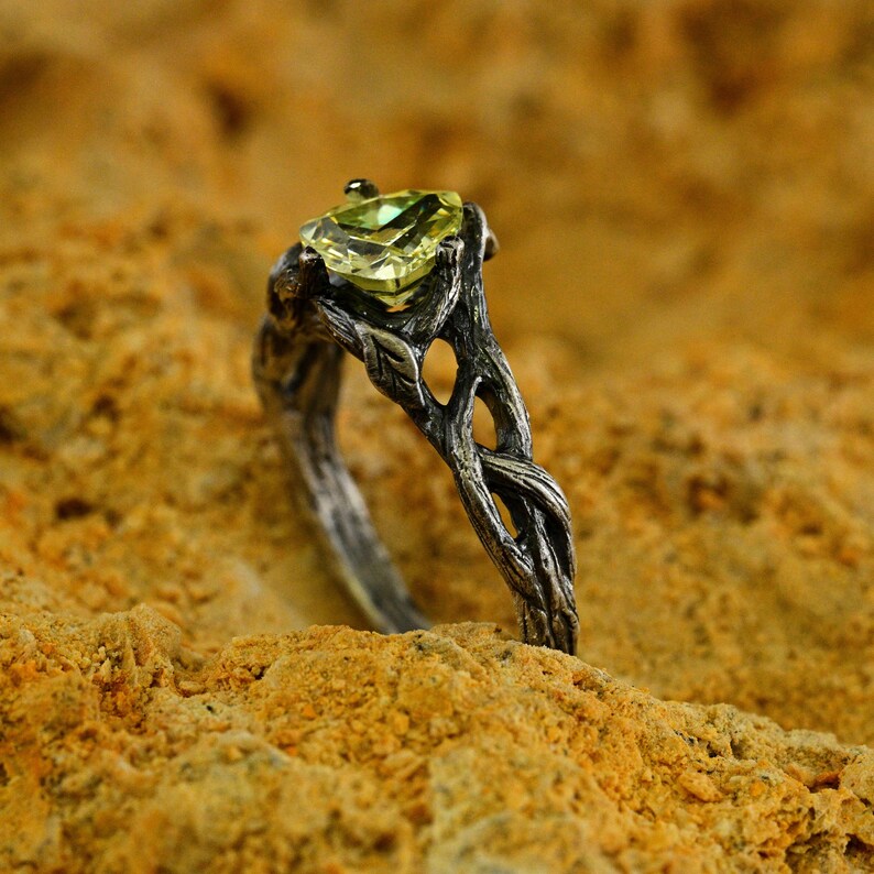 Puede incluir: Un anillo de plata con un dise&ntilde;o de rama retorcida y una piedra preciosa verde engastada en el centro.