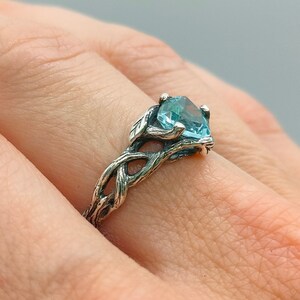 Puede incluir: Un anillo de plata con una piedra preciosa azul engastada en un dise&ntilde;o de rama retorcida.