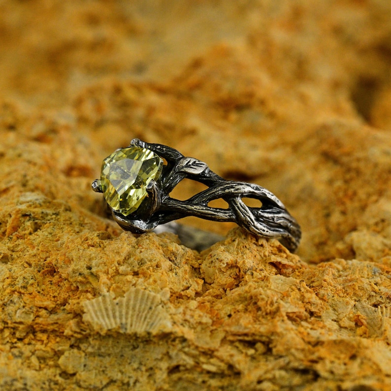 Puede incluir: Un anillo de plata con una piedra preciosa verde engastada en un dise&ntilde;o de rama retorcida.