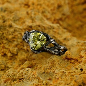 Puede incluir: Un anillo de plata con una piedra preciosa verde engastada en un dise&ntilde;o de rama retorcida.