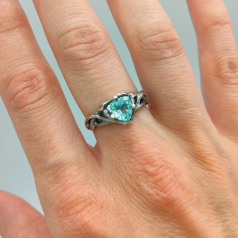 Puede incluir: Un anillo de plata con una banda retorcida y una piedra preciosa azul claro en un engaste triangular.