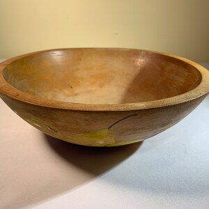 May include: A wooden bowl with a light brown interior and a darker brown rim. The exterior features a painted design of yellow pears with black stems and leaves. The bowl is round and has a smooth finish.