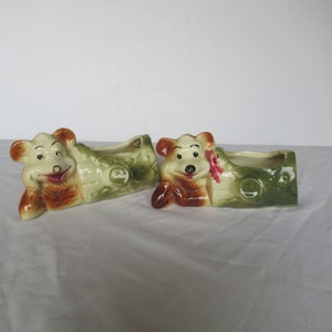 May include: Two ceramic planter pots shaped like a log with a cartoon bear face on each end. The bears are brown and white with black eyes and a red nose. The logs are green and brown with a white background.
