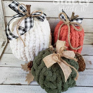 May include: Three handmade, plush pumpkins in cream, coral, and green. Each pumpkin has a twig stem and is adorned with a burlap or buffalo check ribbon bow. Decorative fall-themed items for home decor.