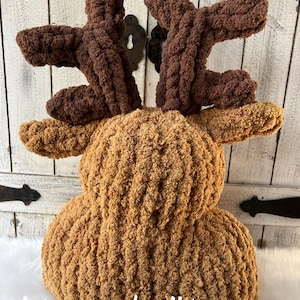 May include: A handmade, plush reindeer pillow in shades of brown. The body is a light brown, while the antlers are a darker brown. The pillow has a textured, chunky knit appearance. The text "stacey made it!" is visible.