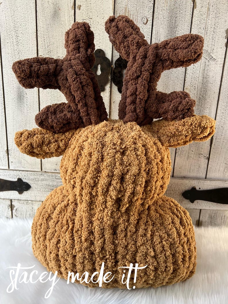 May include: A handmade, plush reindeer pillow in shades of brown. The body is a light brown, while the antlers are a darker brown. The pillow has a textured, chunky knit appearance. The text "stacey made it!" is visible.