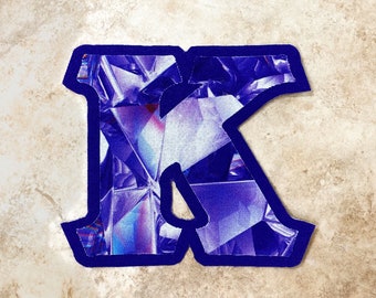 May include: A blue felt letter K with a purple and white geometric pattern.