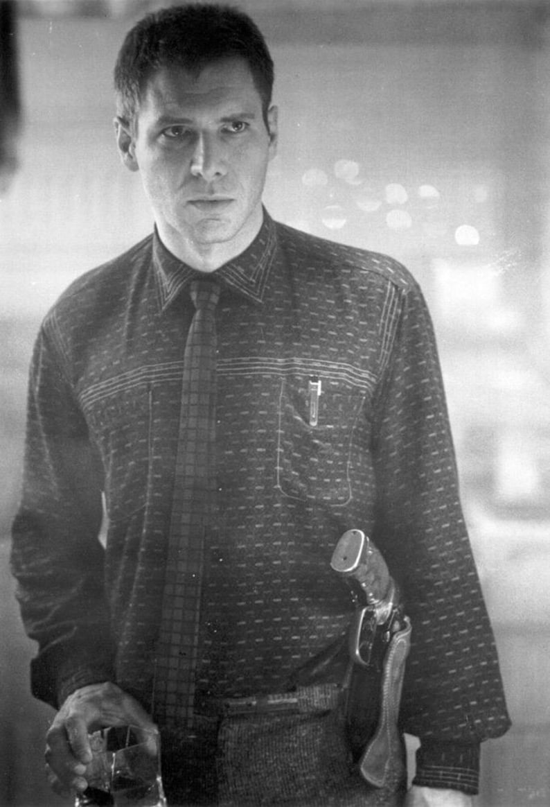 Puede incluir: Imagen en blanco y negro de un hombre con una camisa estampada y corbata. Un bol&iacute;grafo est&aacute; en el bolsillo de la camisa. Una pistola est&aacute; en una funda en la cadera. El hombre sostiene un vaso de l&iacute;quido.