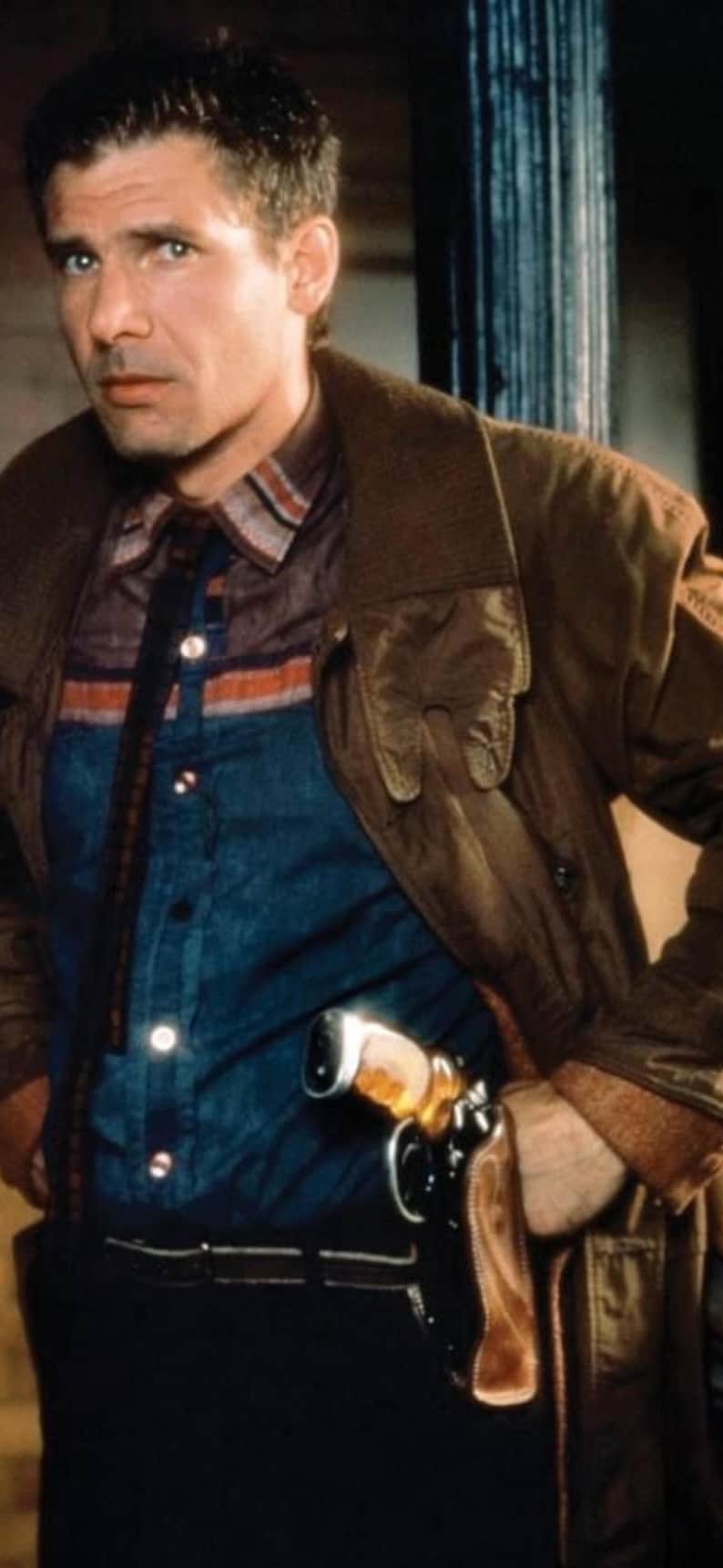 Puede incluir: Un hombre con una chaqueta de cuero marr&oacute;n, camisa azul y pantalones oscuros, con una pistola en una funda. La chaqueta tiene un cuello ancho y la camisa tiene un estampado de rayas. La escena est&aacute; tenuemente iluminada.