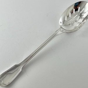 May include: A shiny, silver slotted spoon with an oval bowl and a long, slender handle. The bowl has several rectangular and circular holes. The handle has a decorative design near the bowl and a rounded end.