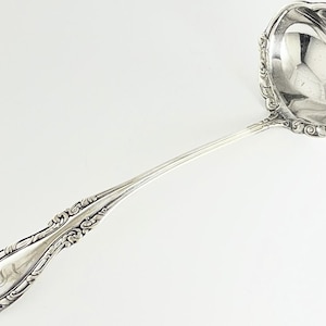 May include: A silver ladle with an ornate handle and a scalloped bowl. The handle features engraved detailing and a monogram. The ladle is designed for serving and has a classic, elegant appearance.