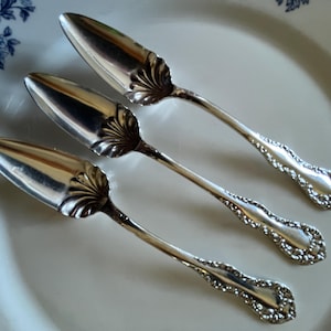 May include: A white ceramic mug with a black handle and the text "But First, Coffee" in a bold, black font. The mug is set against a blurred background, suggesting a cozy setting.