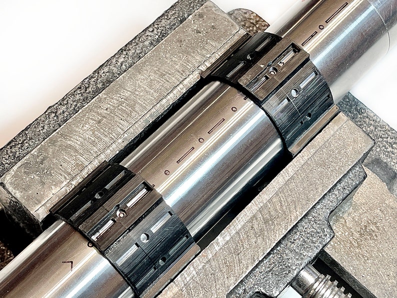 Pode incluir: Close-up de uma haste de metal com duas bra&ccedil;adeiras ajust&aacute;veis pretas. A haste &eacute; mantida em um torno de metal.