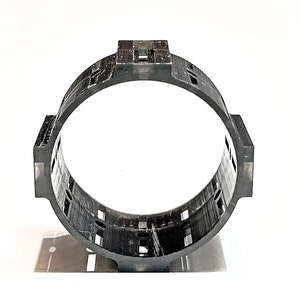 Pode incluir: Um anel de pl&aacute;stico preto com uma s&eacute;rie de furos e ranhuras ao redor da circunfer&ecirc;ncia. O anel &eacute; projetado para ser usado como espa&ccedil;ador ou suporte.