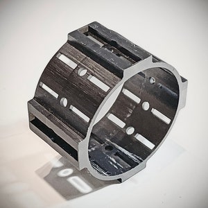 Pode incluir: Anel de pl&aacute;stico preto com v&aacute;rias ranhuras e furos. O anel &eacute; projetado para segurar um objeto redondo no lugar.