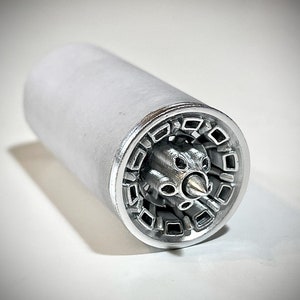 Puede incluir: Un modelo de motor a reacción de metal plateado con un diseño detallado. El motor es cilíndrico con una abertura circular en un extremo, revelando una estructura interna compleja.