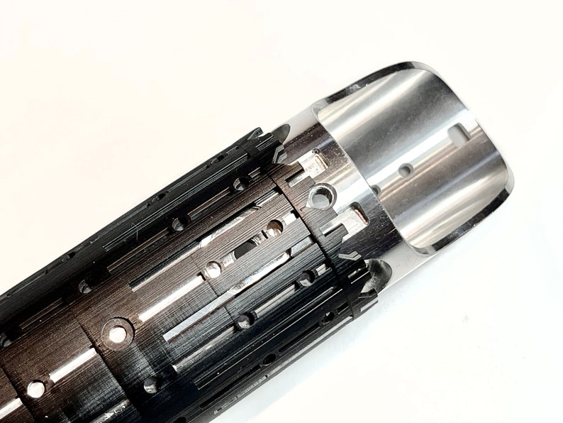 Pode incluir: Um close-up de um objeto de metal preto e prata com uma s&eacute;rie de pequenos orif&iacute;cios e ranhuras. O objeto &eacute; cil&iacute;ndrico e tem uma extremidade arredondada.