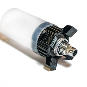 Puede incluir: Una botella de plástico transparente con una tapa negra y una boquilla plateada. La tapa tiene un diseño texturizado y una pequeña perilla en el lateral.