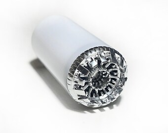May include: A silver-colored metal object with a cylindrical shape and a detailed, intricate design on one end. The object is made of metal and has a smooth, polished finish.