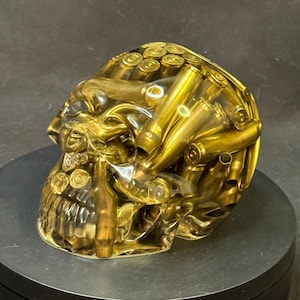 May include: A gold skull sculpture made of clear resin filled with gold-colored bullet casings.