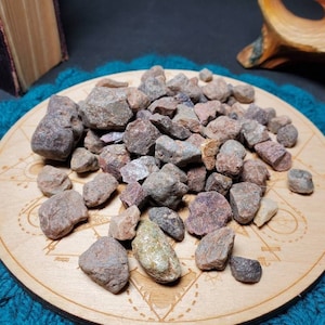 May include: A pile of small, rough, red and brown stones on a wooden circular tray with a decorative pattern. The tray is on a blue surface.