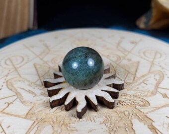 May include: A green and blue gemstone sphere resting on a wooden stand with a starburst design.
