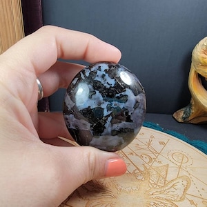 May include: A polished black and white gemstone with a swirling pattern. The stone is oval shaped and has a smooth, glossy finish.