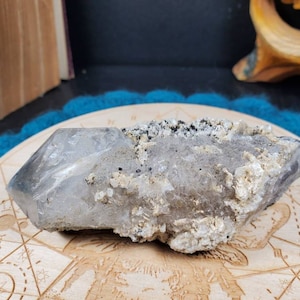 May include: A large, clear quartz crystal with a gray, cloudy, and textured surface. The crystal is partially embedded in a matrix of smaller, white crystals.