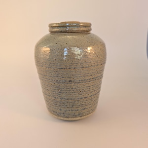 May include: A ceramic jar with a light grey glaze and a speckled finish. The jar has a rounded body and a wide mouth.