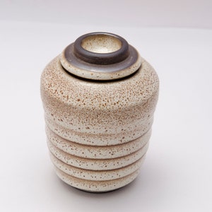 May include: A white ceramic jar with a brown speckled glaze and a dark brown lid. The jar has a textured, ribbed design.