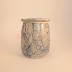 Puede incluir: Un tarro de cerámica con tapa. El tarro es cilíndrico con la parte superior e inferior redondeadas. Presenta un patrón de burbujas azules y blancas. La tapa es del mismo color y diseño. El tarro es adecuado para guardar objetos pequeños.