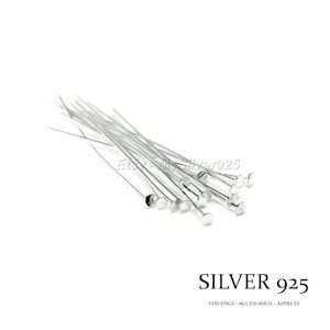 Peut inclure: Gros plan sur un groupe d'épingles à tête en argent 925. Les épingles sont disposées en un tas lâche sur une surface blanche. Les épingles mesurent environ 2,5 cm de long et ont une petite tête ronde.