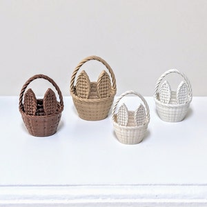 Può includere: Cinque cestini intrecciati in miniatura con manici a forma di orecchie di coniglio. I cestini sono di colore marrone, beige e bianco.